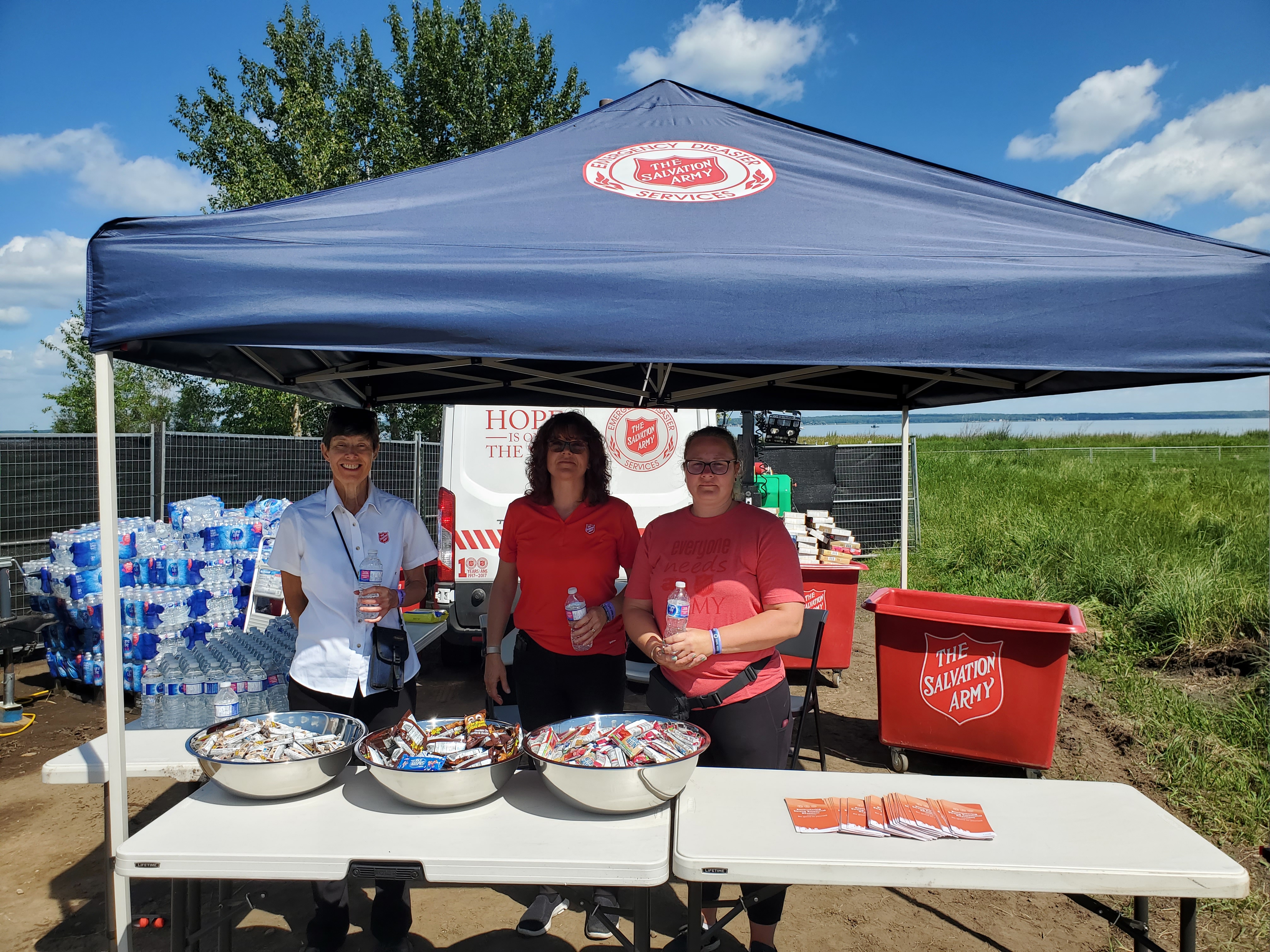 Three Army employees standing under a tent giving out snacks and water bottles.