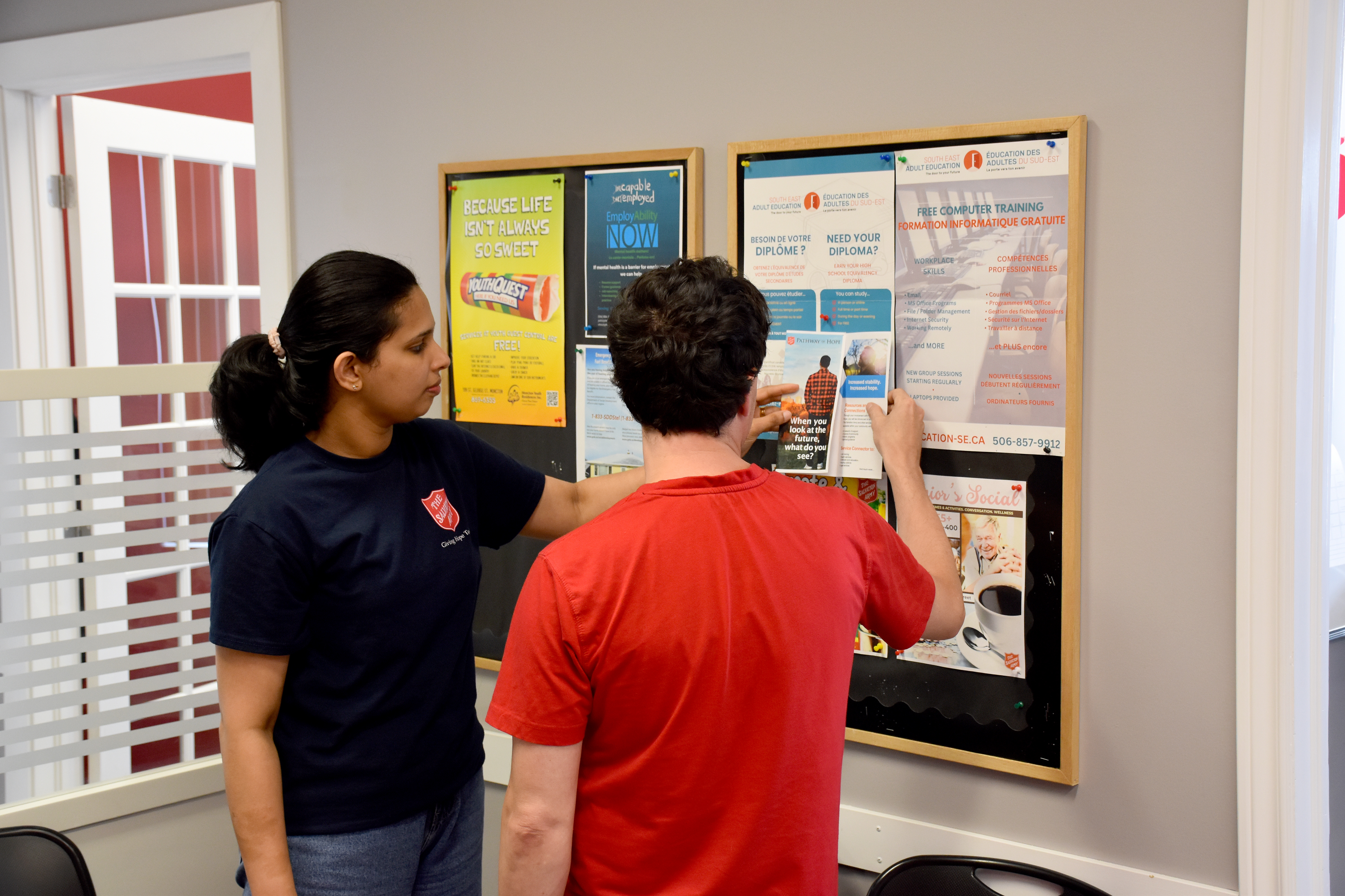 Two Salvation Army employees discussing posters on a bulletin board.