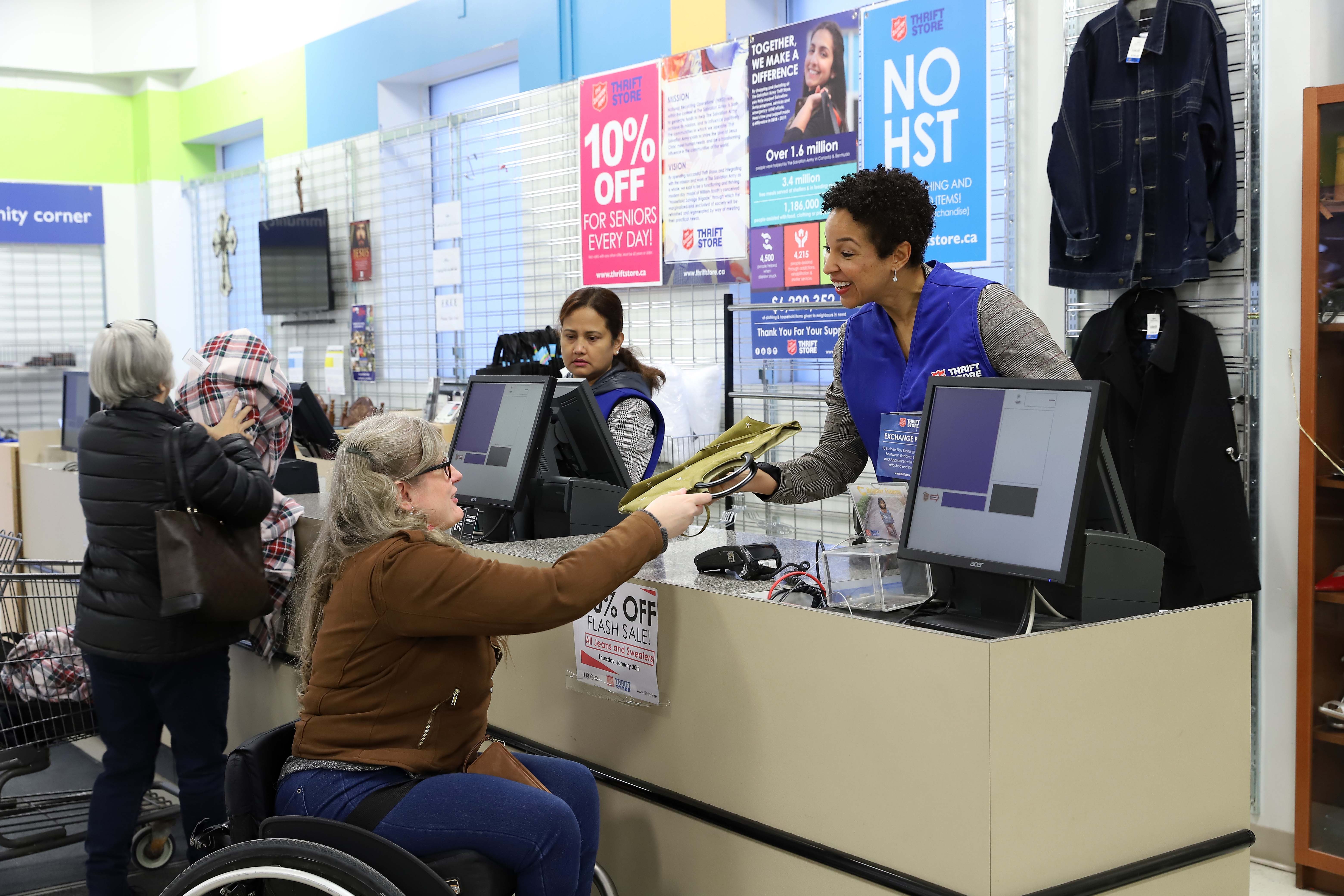 A picture of a thrift store employee checking out a client who is sitting in a wheelchair.